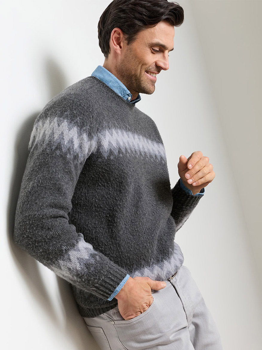 A man wearing a fuzzy, grey Peter Millar Après-Ski Crewneck Sweater in Fossil with a light grey zigzag pattern over a light blue collared shirt and light-colored trousers.