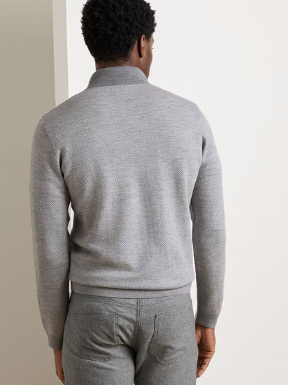 A person stands facing away from the camera, wearing a Peter Millar Ashland Quarter-Zip Sweater in Gale Grey paired with matching gray pants, in front of a neutral background.