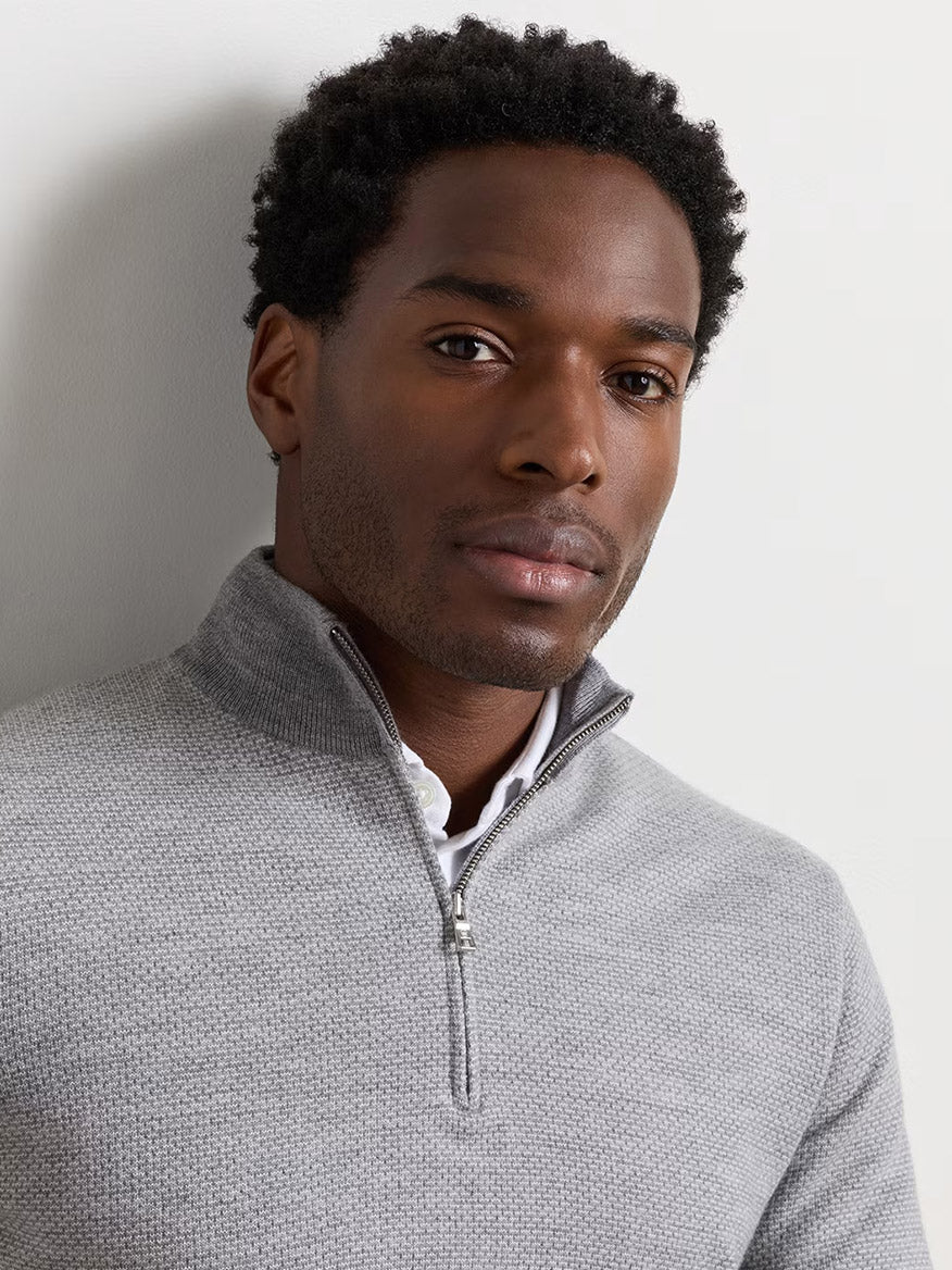 A man faces forward against a plain light background, wearing the Peter Millar Ashland Quarter-Zip Sweater in Gale Grey—a light grey midweight sweater with a tailored fit—layered over a white collared shirt.