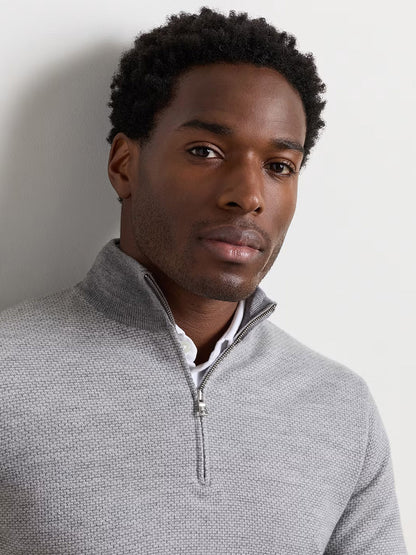 A man faces forward against a plain light background, wearing the Peter Millar Ashland Quarter-Zip Sweater in Gale Grey—a light grey midweight sweater with a tailored fit—layered over a white collared shirt.