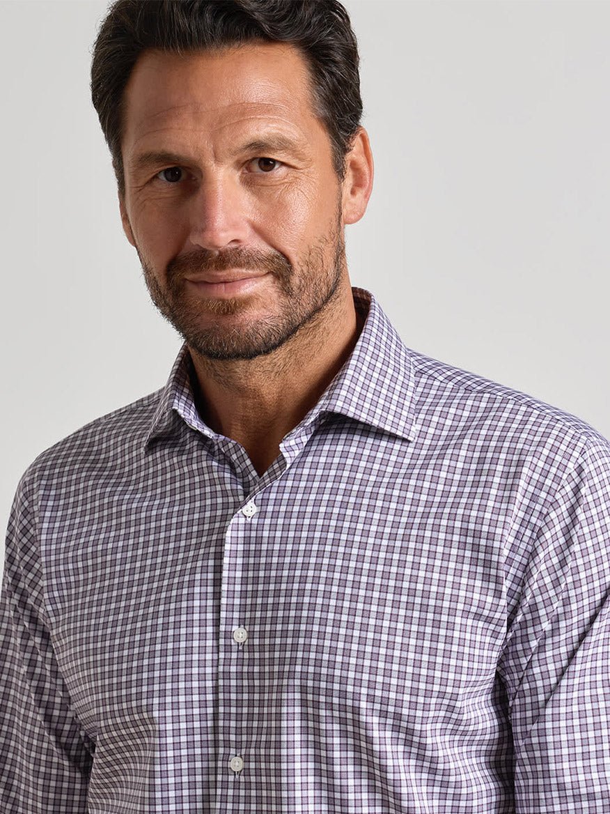 Man with short dark hair and beard wearing the Peter Millar Atlas Crown Lite Cotton-Stretch Sport Shirt in Grapeseed—a classic fit purple and white checkered button-up crafted from easy-care fabric—standing against a plain light background.