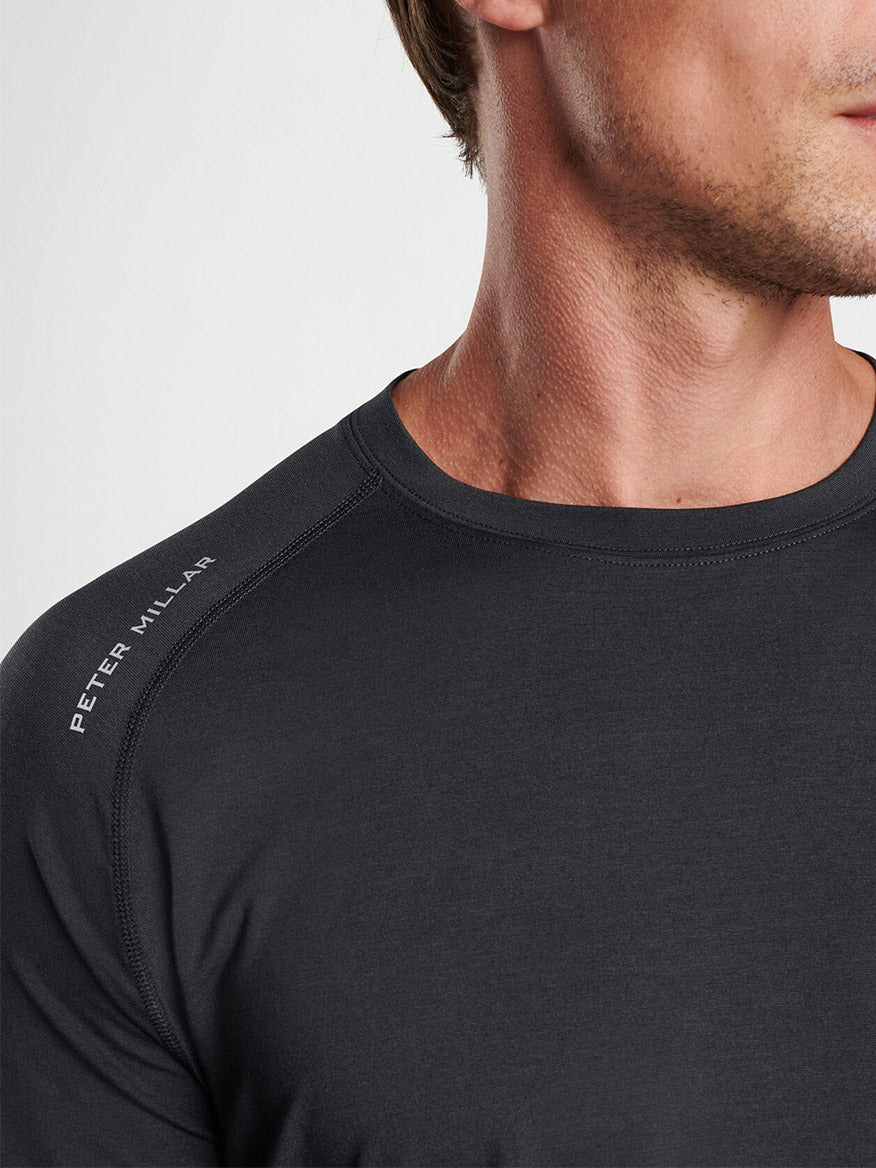 Close-up of a man wearing a Peter Millar Aurora Performance Long-Sleeve T-Shirt in Black with the "Peter Millar" logo on the sleeve and UPF 50+ sun protection.