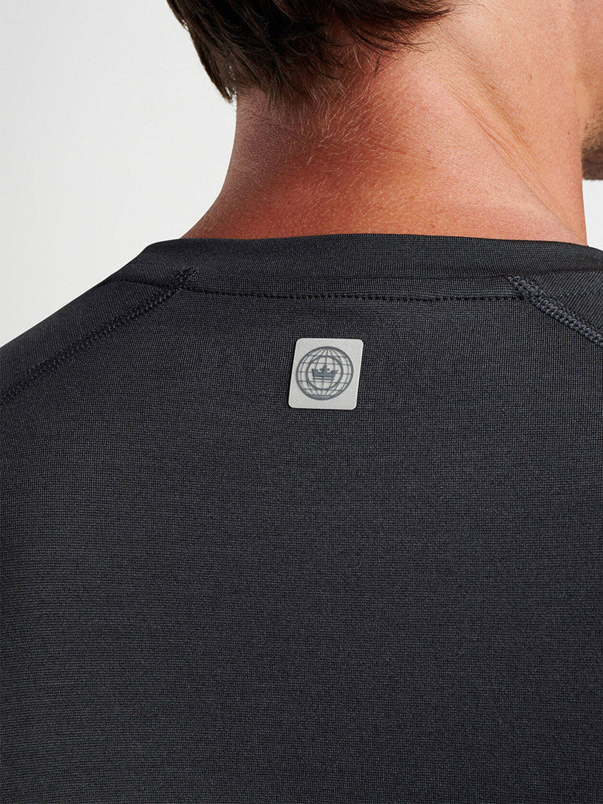 Close-up of a man's upper back wearing a Peter Millar Aurora Performance Long-Sleeve T-shirt in Black with UPF 50+ sun protection, featuring a small, square white label on the neckline.