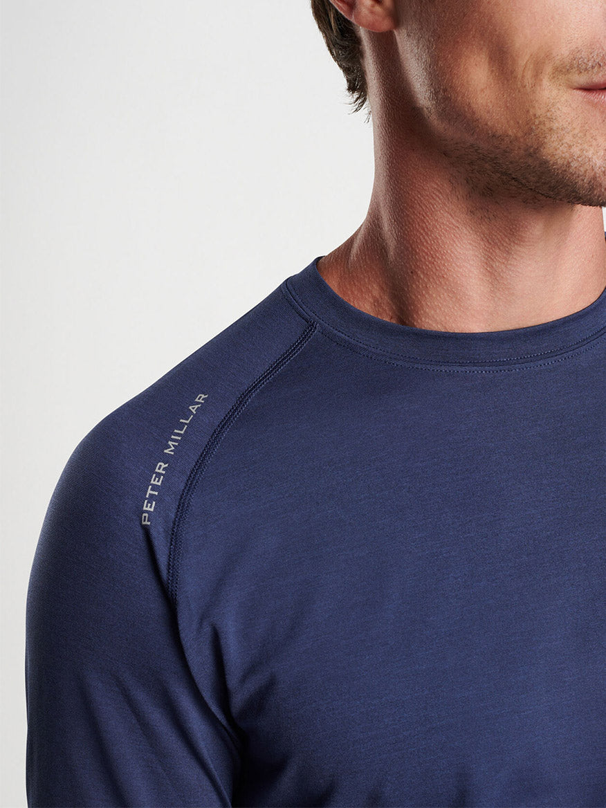 Partial profile of a man wearing a blue T-shirt with the "Peter Millar Aurora Performance Long-Sleeve T-Shirt in Navy" logo on the sleeve, designed for the gym with performance yarn.