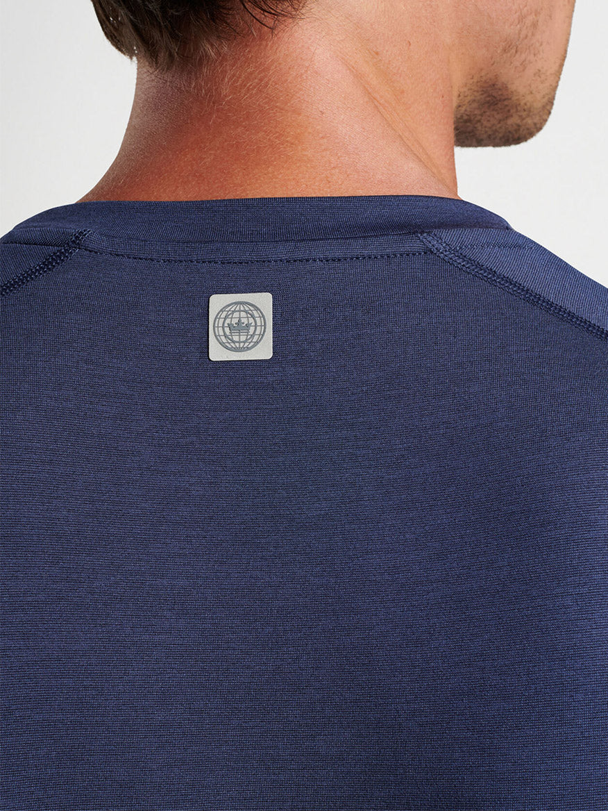 A close-up view of a man's upper back wearing a Peter Millar Aurora Performance Long-Sleeve T-Shirt in Navy with a gym brand logo on the nape, crafted from performance yarn.