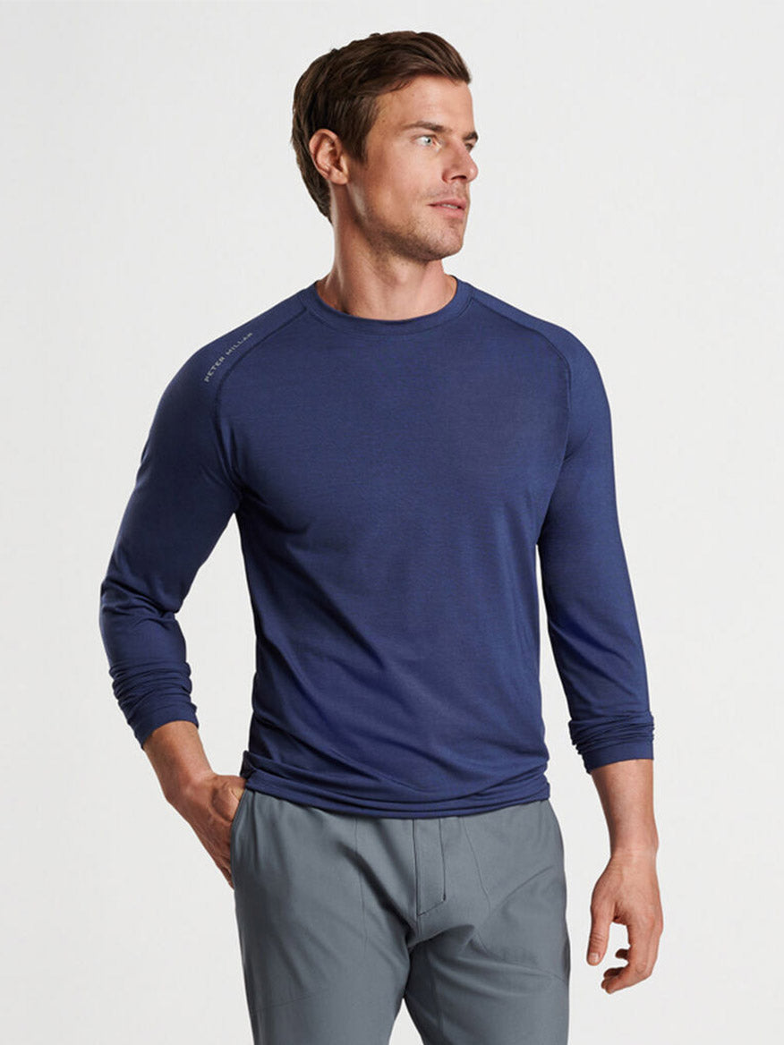 A man wearing a Peter Millar Aurora Performance Long-Sleeve T-Shirt in Navy made of performance yarn and grey pants.