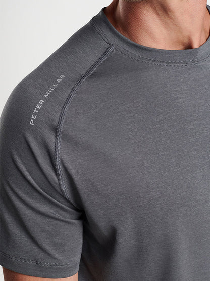 Close-up view of a person wearing a grey Peter Millar Aurora Performance T-shirt in Iron with "Peter Millar" text on the shoulder.