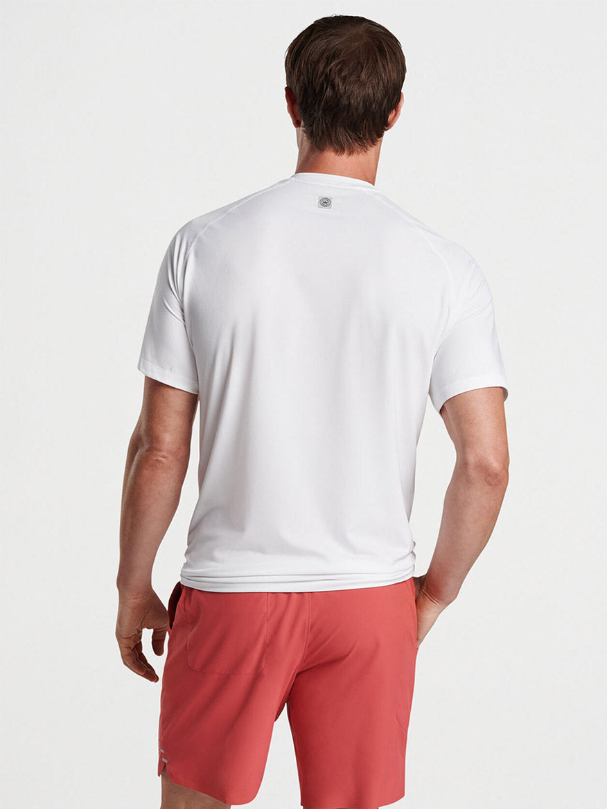 Man standing with his back to the camera, wearing a Peter Millar Aurora Performance T-Shirt in White made of performance yarn and red shorts.