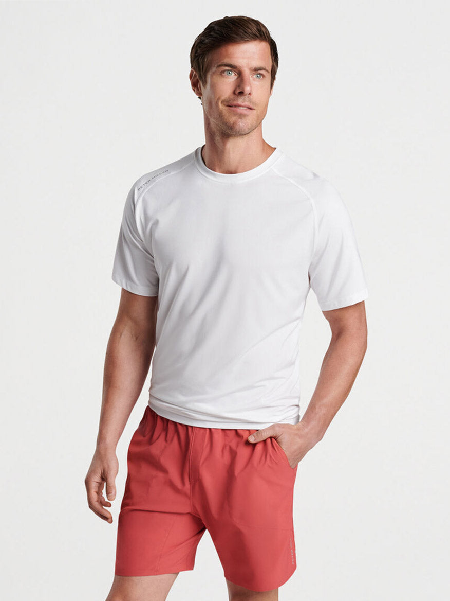 Man posing in a gym with a Peter Millar Aurora Performance T-Shirt in White and red shorts.