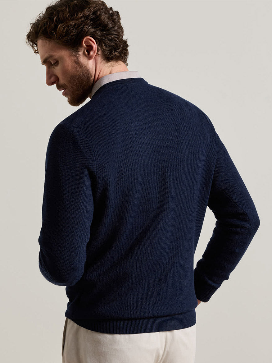 A man stands with his back to the camera, wearing the Peter Millar Autumn Crest Honeycomb Crewneck Sweater in Navy, styled in a classic fit with light-colored pants against a plain background.