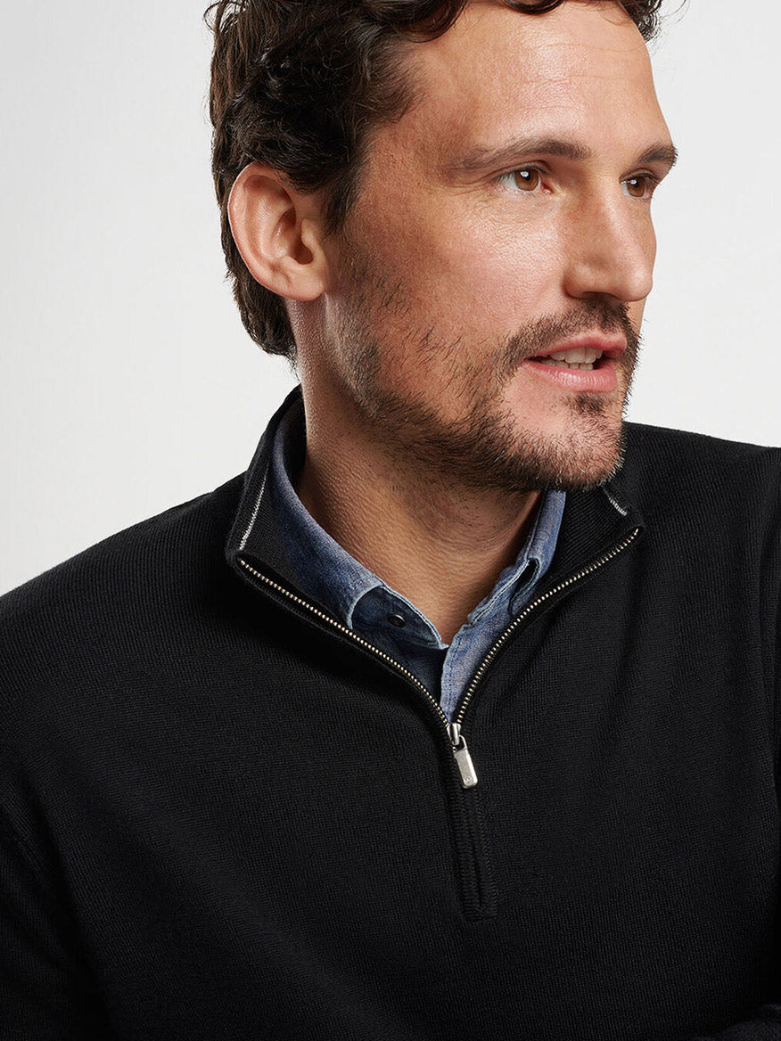 A man with brown hair and a beard wears a black Peter Millar Autumn Crest Quarter-Zip over a blue shirt, looking to the side.