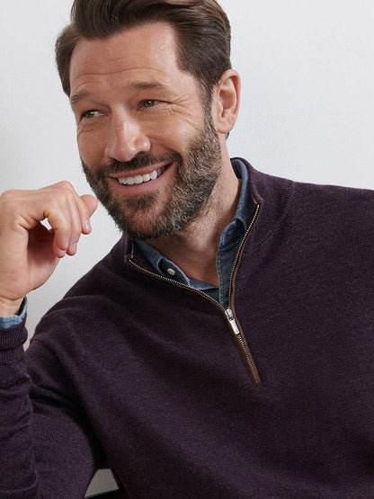 A bearded man smiles while seated, wearing the Peter Millar Autumn Crest Suede Trim Quarter-Zip in Midnight Grape, styled over a collared shirt.