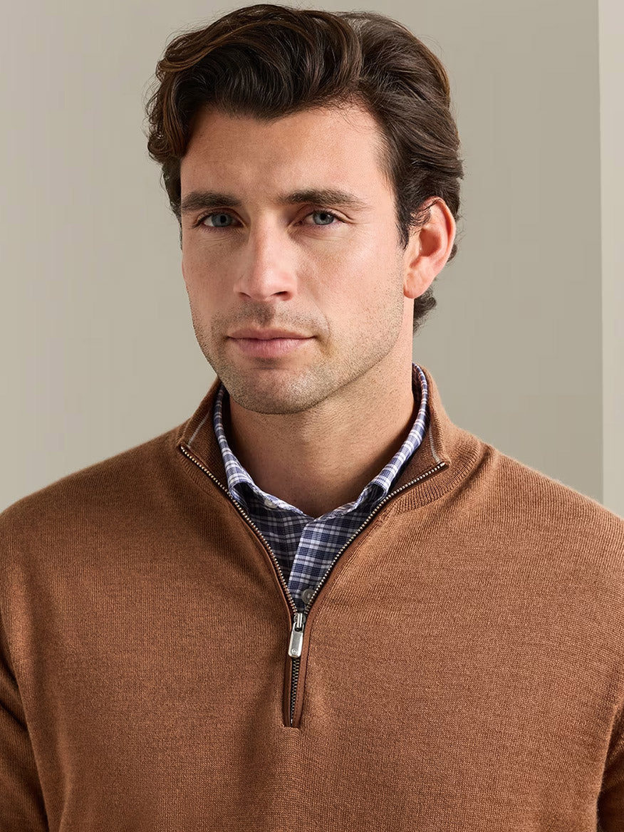 Man with brown hair wears the Peter Millar Autumn Crest Suede Trim Quarter-Zip in Dark Amber over a checkered shirt, standing indoors against a plain beige background.