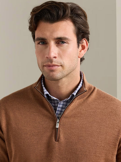 Man with brown hair wears the Peter Millar Autumn Crest Suede Trim Quarter-Zip in Dark Amber over a checkered shirt, standing indoors against a plain beige background.