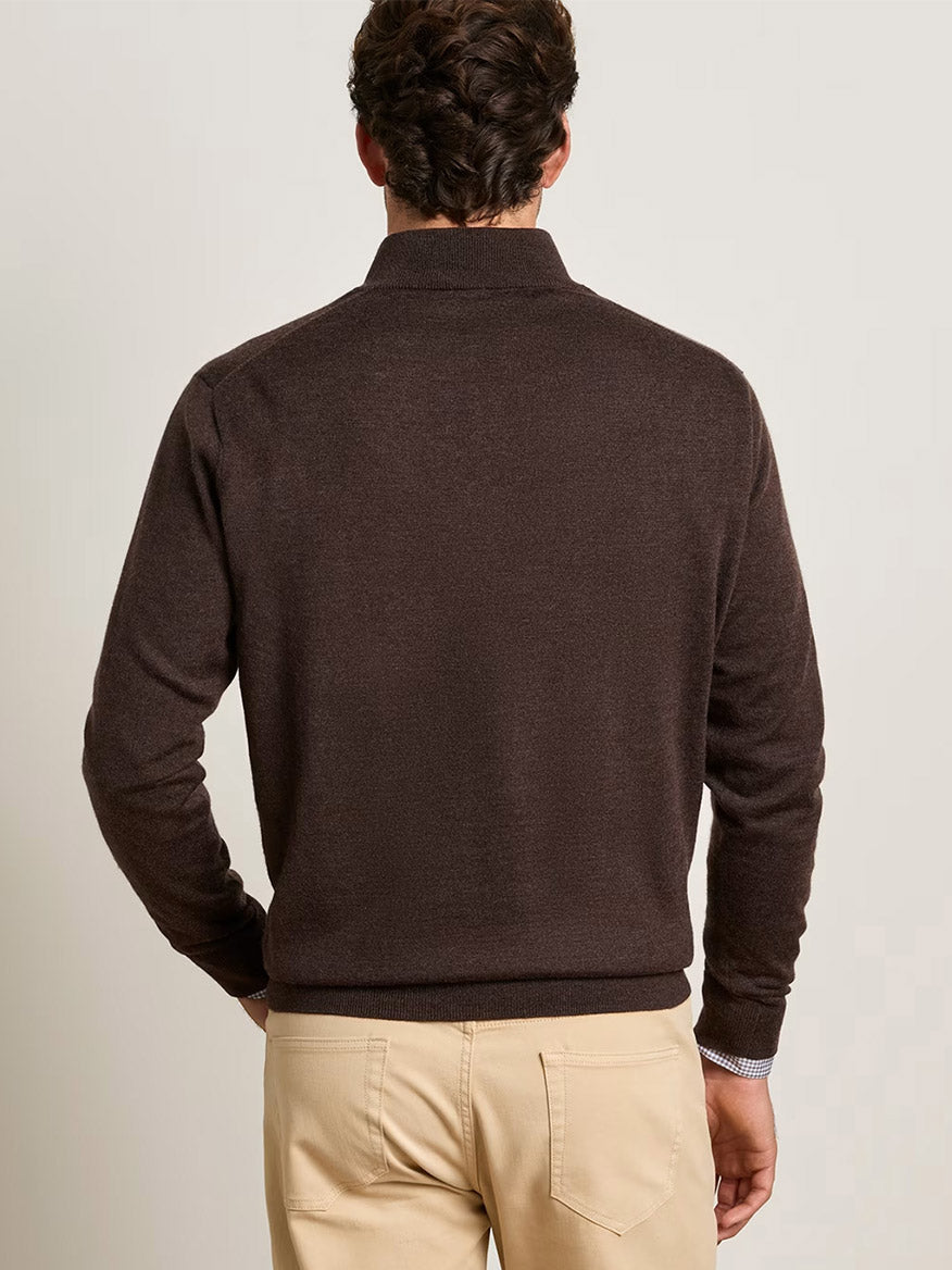 A man facing away, wearing the Peter Millar Autumn Crest Suede Trim Quarter-Zip in French Press and beige pants, stands against a plain light-colored background.