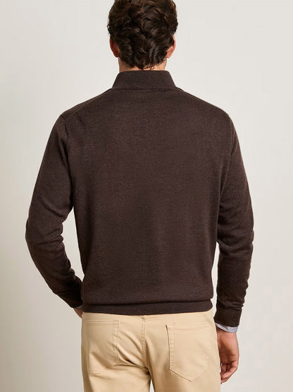 A man facing away, wearing the Peter Millar Autumn Crest Suede Trim Quarter-Zip in French Press and beige pants, stands against a plain light-colored background.