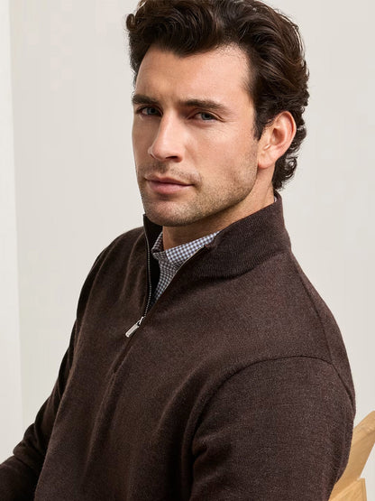 A man with short brown hair is seated and looking slightly to the side, wearing a collared shirt beneath the Peter Millar Autumn Crest Suede Trim Quarter-Zip in French Press (a classic-fit, dark brown Merino sweater).