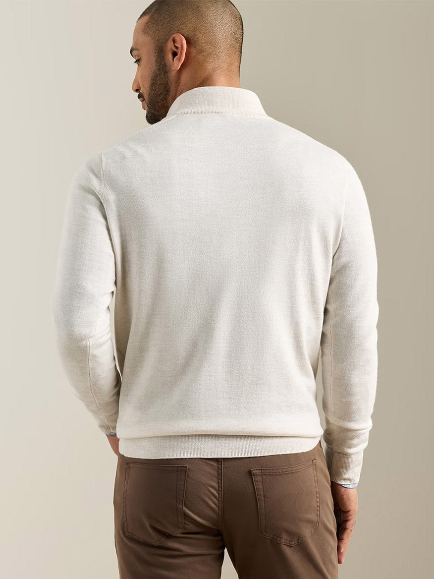 A man facing away, wearing a Peter Millar Autumn Crest Suede Trim Quarter-Zip in Ivory and brown pants, standing against a plain beige background.