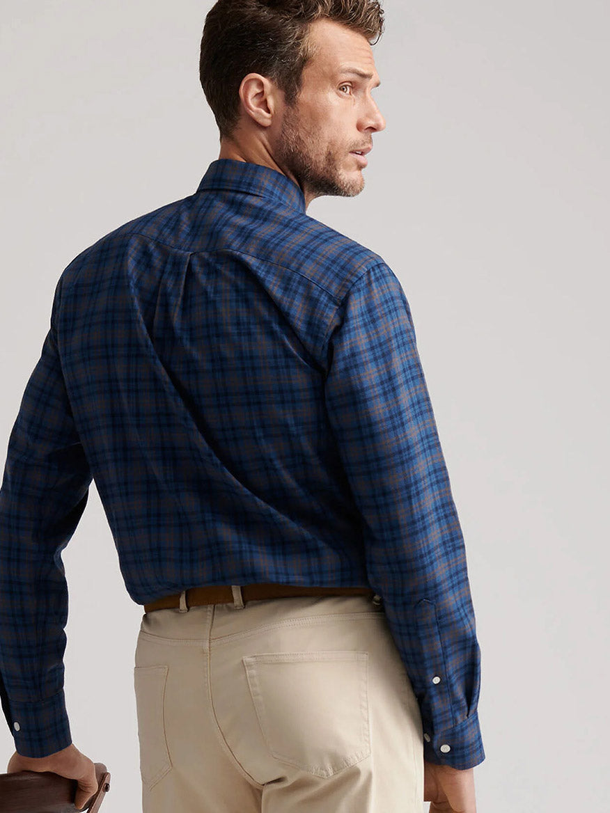 A man wearing a blue Peter Millar Bar Harbor Performance Flannel Sport Shirt in Blue Haze and beige pants stands looking over his shoulder.