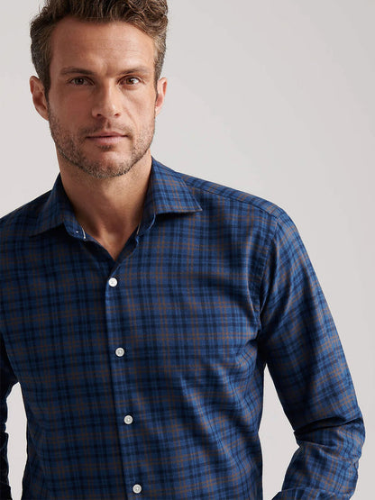 A man wears the Peter Millar Bar Harbor Performance Flannel Sport Shirt in Blue Haze, made from lightweight performance fibers, standing against a plain light background and looking at the camera.