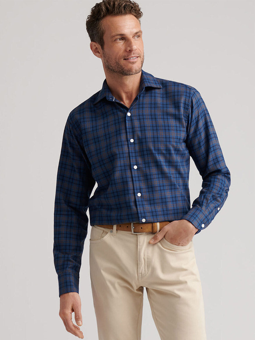 A man wears the Peter Millar Bar Harbor Performance Flannel Sport Shirt in Blue Haze with beige pants, standing with one hand in his pocket against a plain light background.