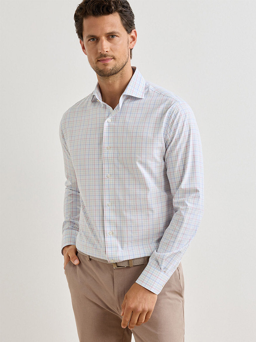 A man wearing a Peter Millar Basin Performance Poplin Sport Shirt in multi stands against a plain light background, enjoying the comfort of performance fabric with UPF 50+ protection and beige pants.