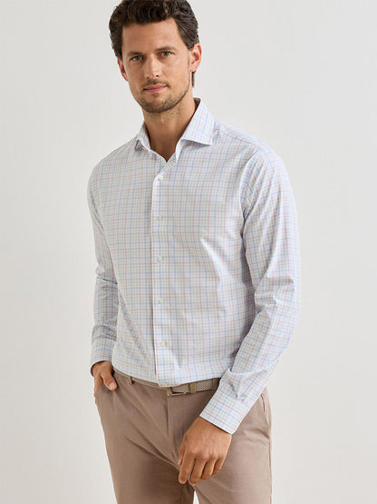 A man wearing a Peter Millar Basin Performance Poplin Sport Shirt in multi stands against a plain light background, enjoying the comfort of performance fabric with UPF 50+ protection and beige pants.
