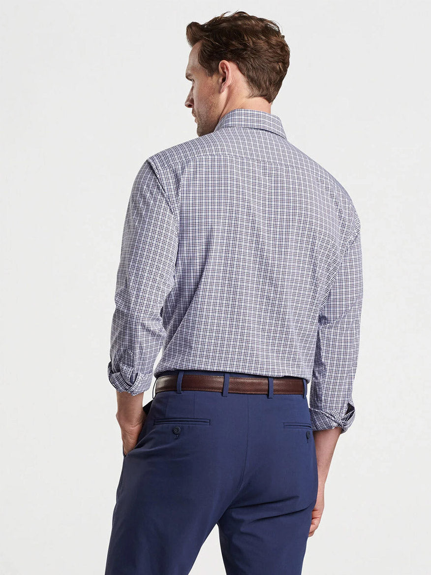 A man is seen from behind, wearing the Peter Millar Berkshire Performance Poplin Sport Shirt in Navy tucked into blue trousers secured with a brown belt.