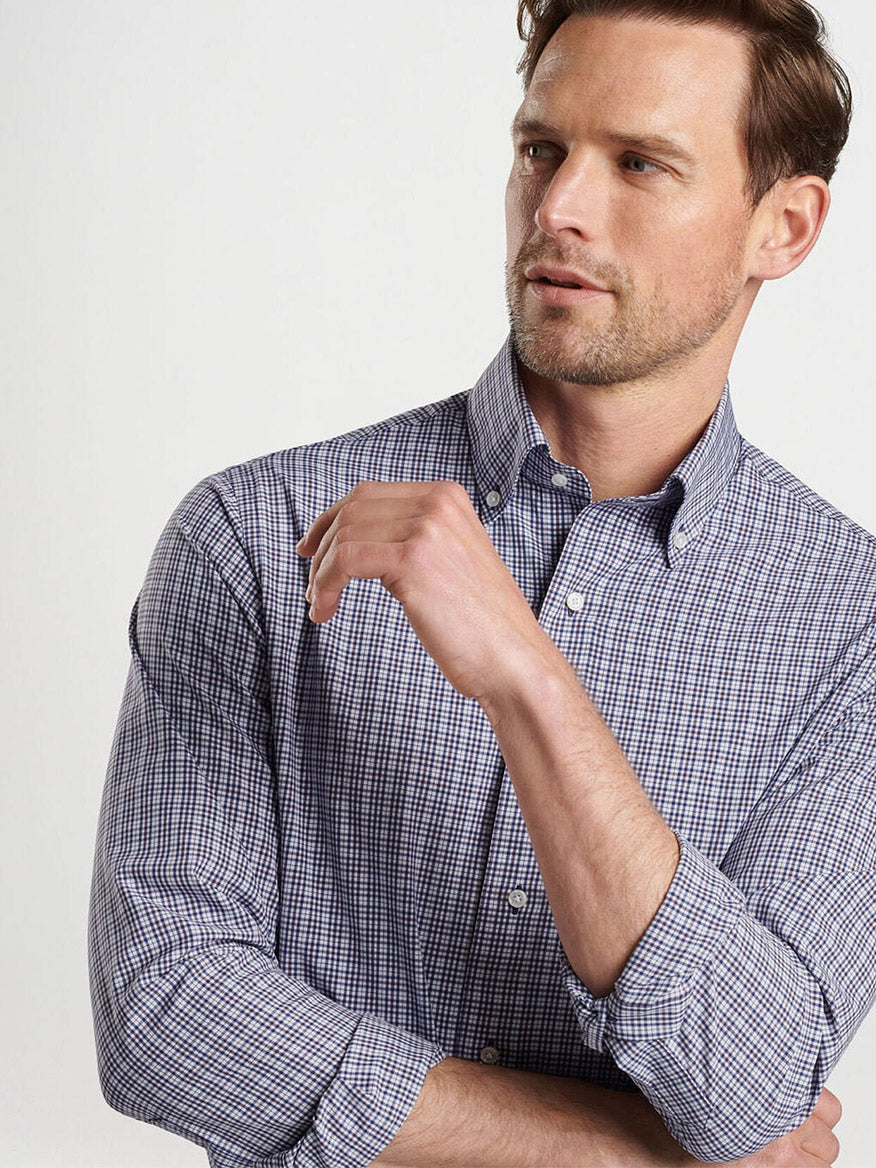 A man in a Peter Millar Berkshire Performance Poplin Sport Shirt in Navy, with rolled-up sleeves and soft performance fabric, is looking to his left, crossing one arm over his chest.