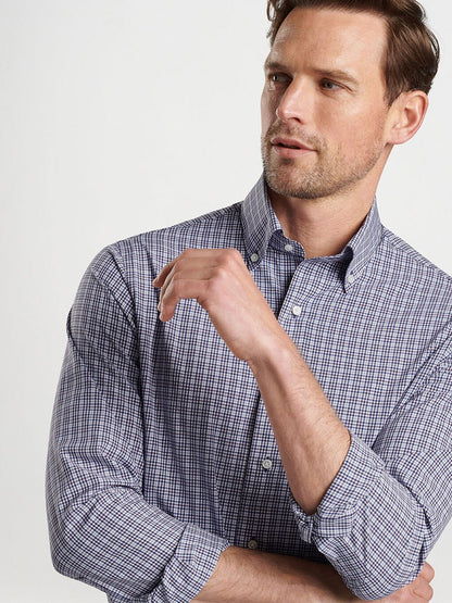 A man in a Peter Millar Berkshire Performance Poplin Sport Shirt in Navy, with rolled-up sleeves and soft performance fabric, is looking to his left, crossing one arm over his chest.