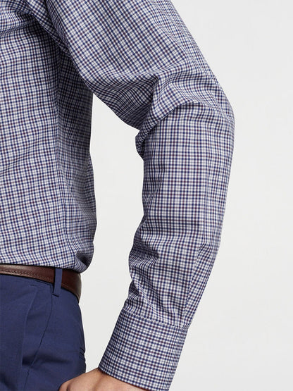 Close-up of a person wearing the Peter Millar Berkshire Performance Poplin Sport Shirt in Navy, featuring long sleeves and checkered design with UPF 50+ sun protection, paired with a brown belt and blue pants, showing their right arm bent at the elbow.