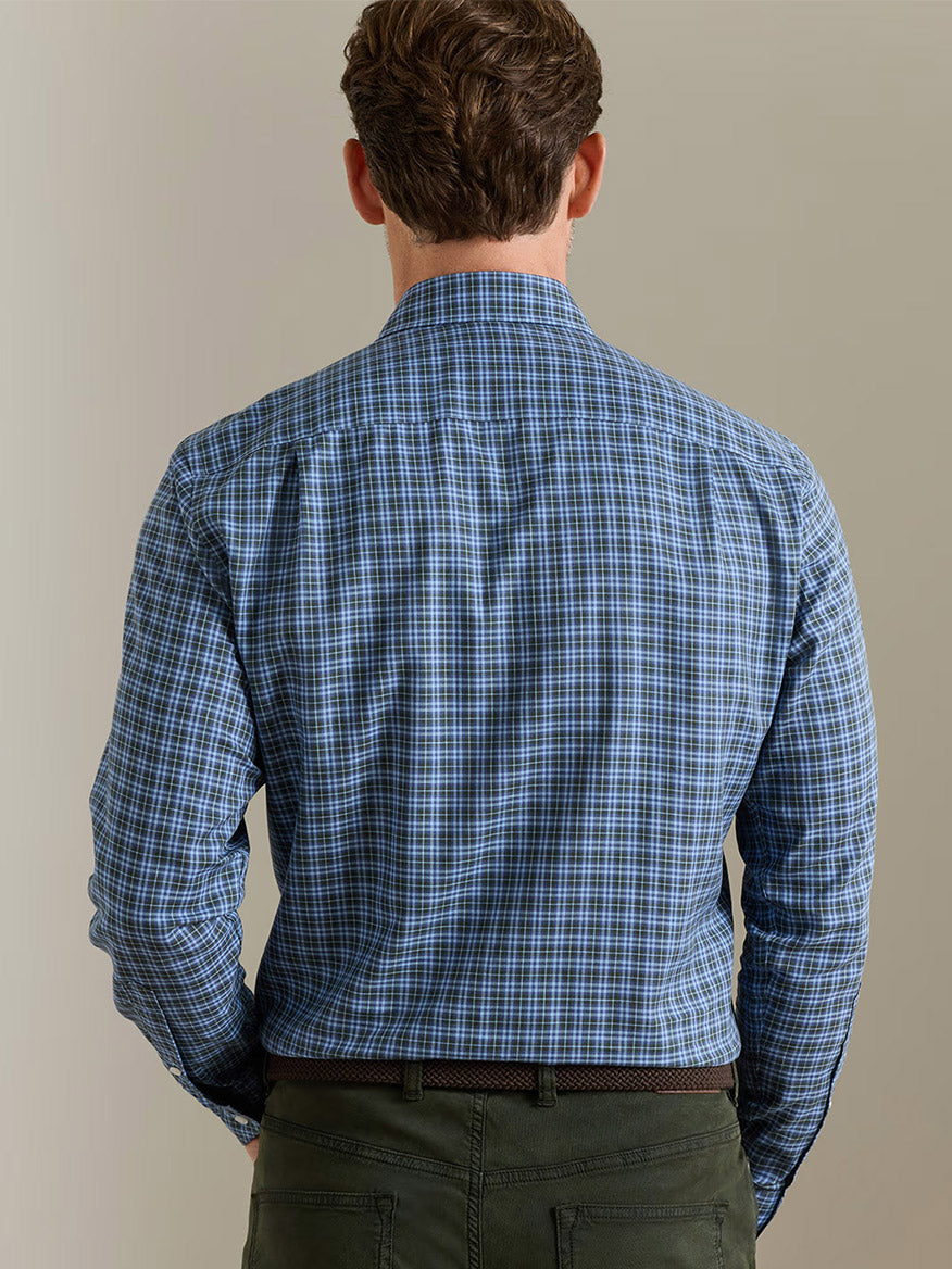A man stands with his back to the camera, wearing the Peter Millar Bernard Cotton Sport Shirt in Windy Blue paired with green pants, set against a neutral background.