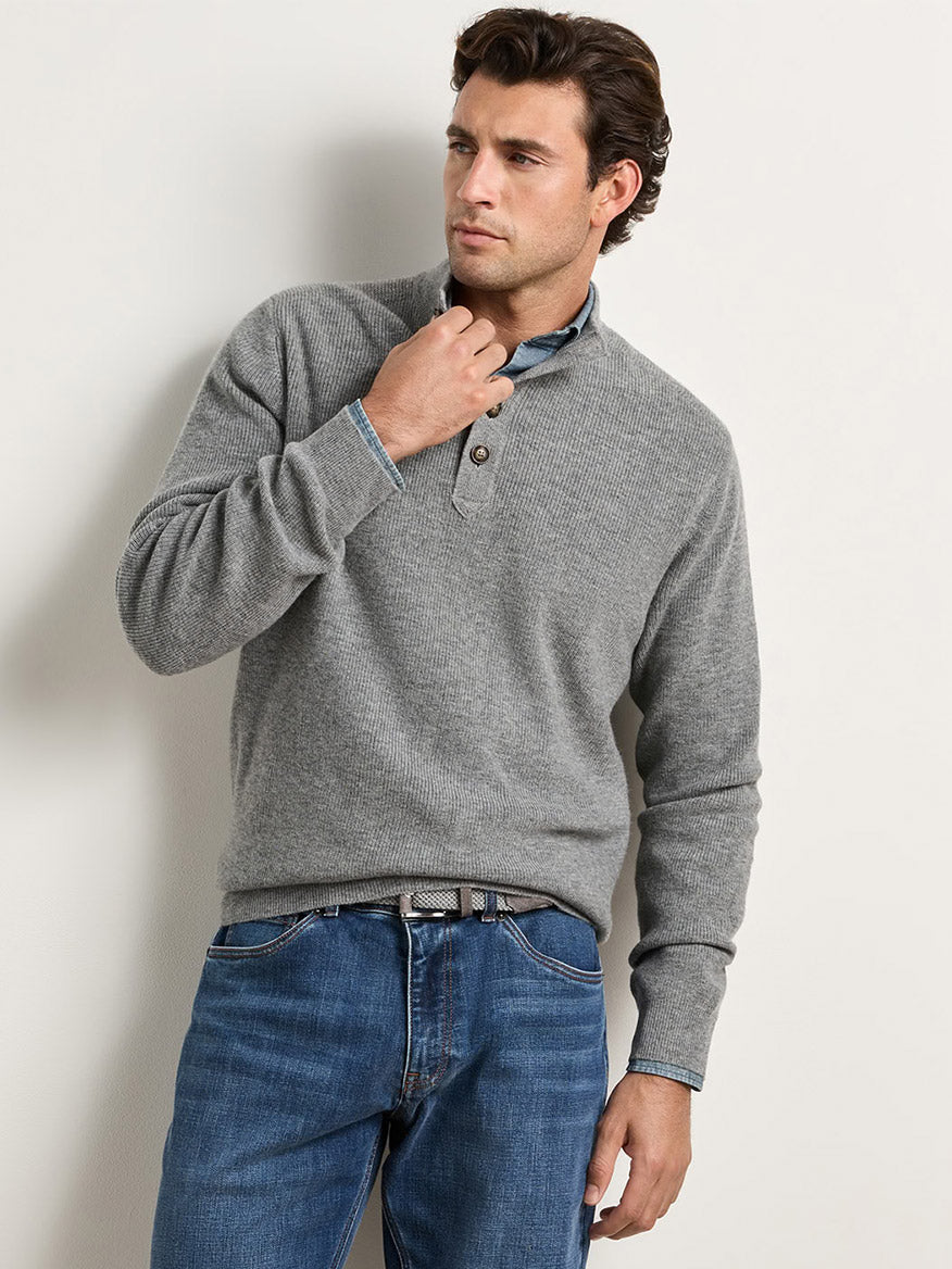 A man wearing a grey Peter Millar Blackburn Button-Mock Sweater in Oslo Grey over a collared shirt and blue jeans.