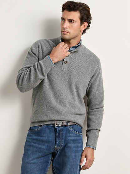 A man wearing a grey Peter Millar Blackburn Button-Mock Sweater in Oslo Grey over a collared shirt and blue jeans.
