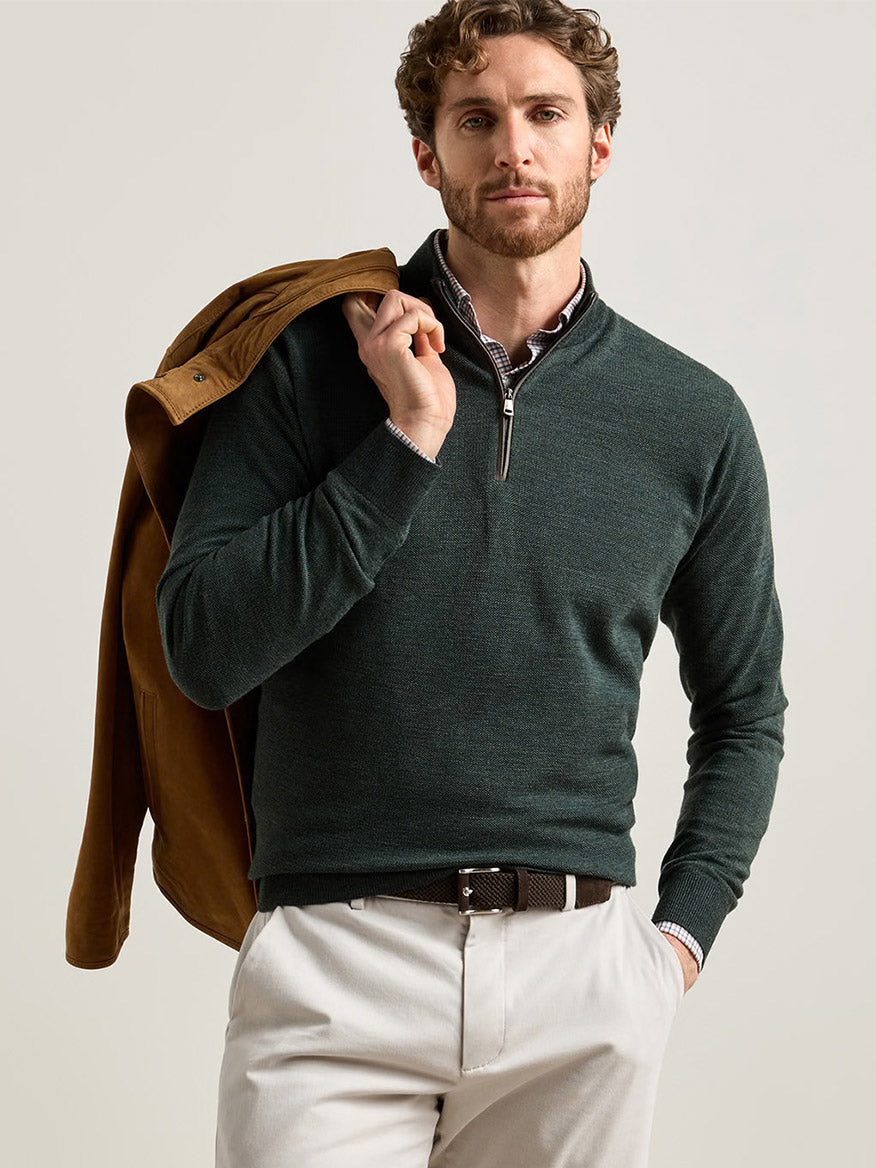 A man wearing a Peter Millar Blair Birdseye Quarter-Zip Sweater in Pine Brook over a plaid button-down shirt, with a tan jacket draped over his shoulder.