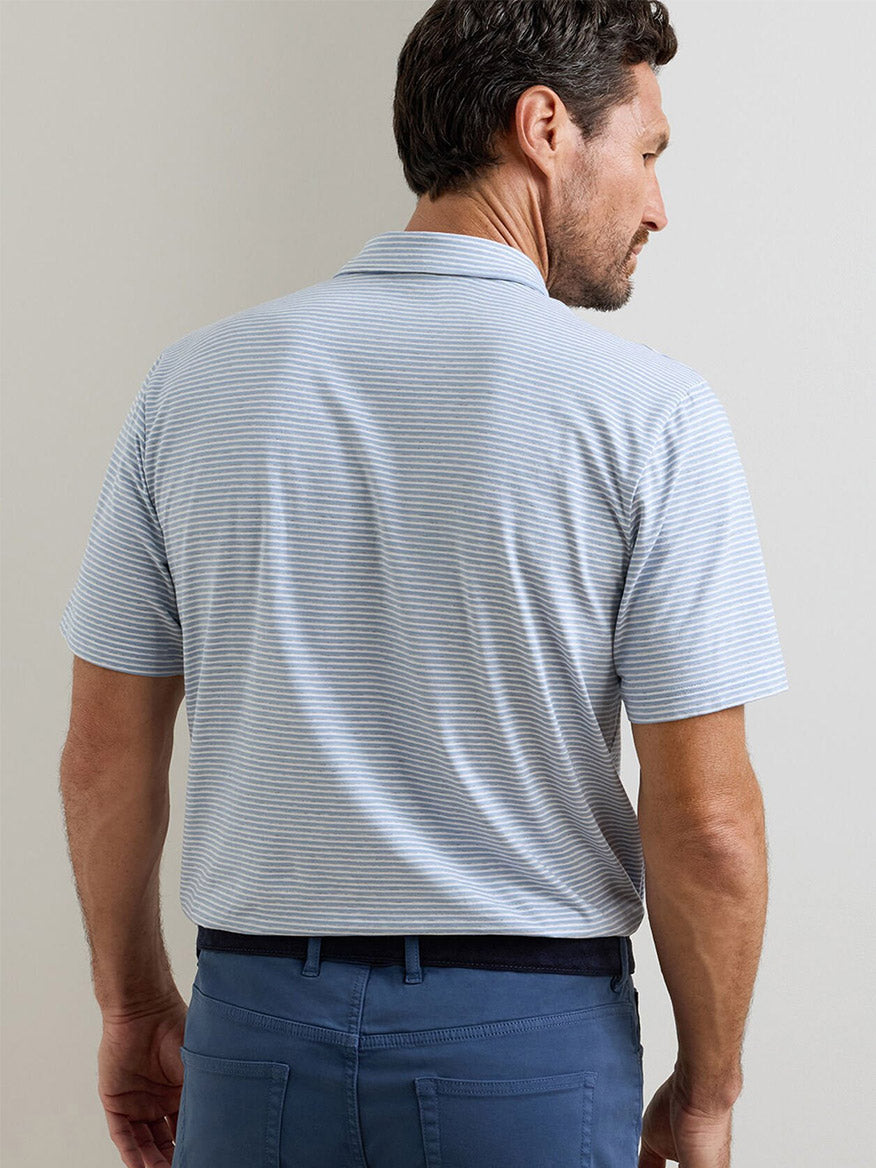 A man wearing a Peter Millar Calvert Crown Flex Cotton Polo in Cloudy Blue and blue pants stands facing away from the camera.