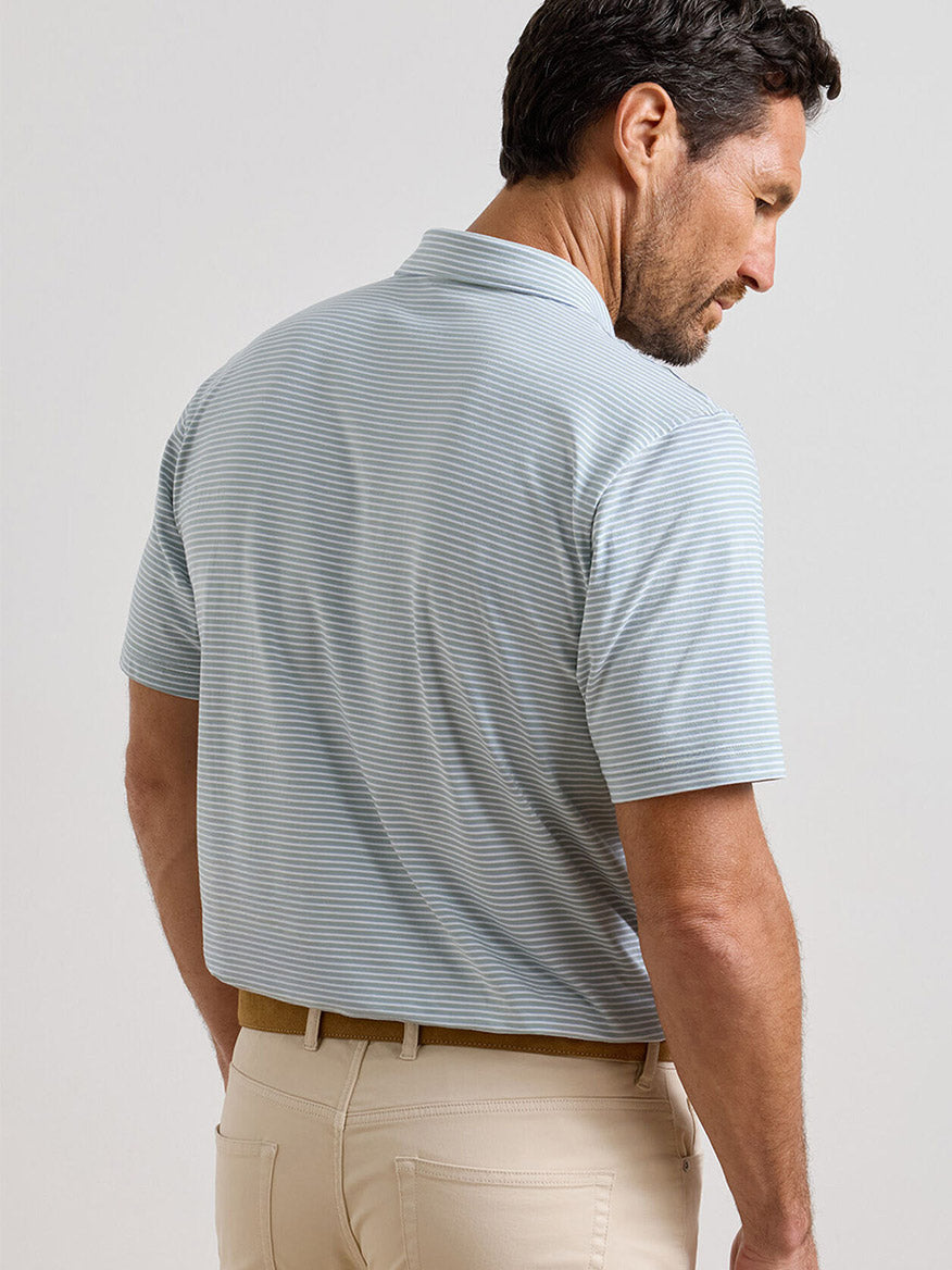 A man with short dark hair, shown from the back and head turned slightly, wears the Peter Millar Calvert Crown Flex Cotton Polo in Grandview (light blue stripes) with beige pants.
