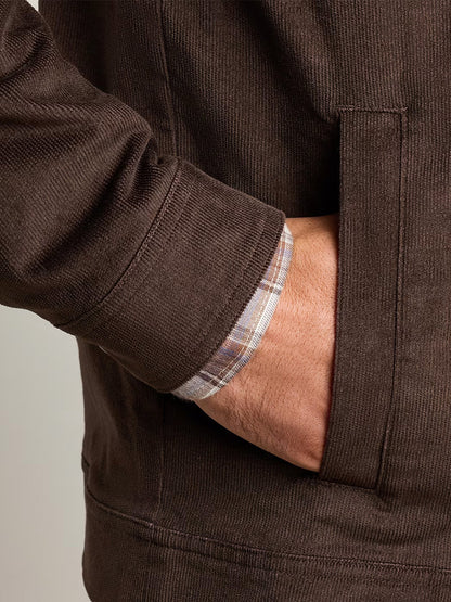 Wearing the Peter Millar Camden Corduroy Jacket in French Press, an individual with a plaid shirt cuff showing slips their right hand into the jacket pocket, highlighting lightweight layering and a classic fit.