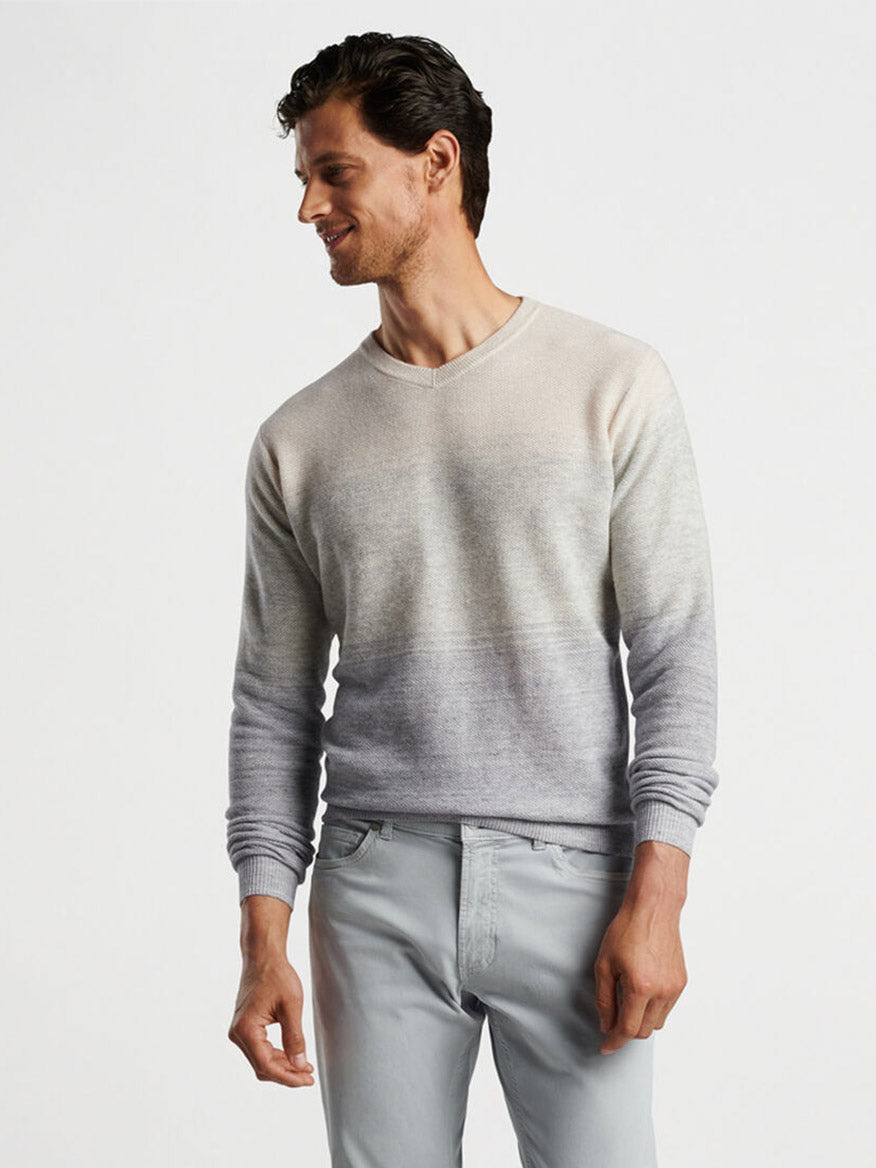 A man in a Peter Millar Camden High V Striped Sweater in British Grey and pale gray pants, smiling slightly as he looks to his left.