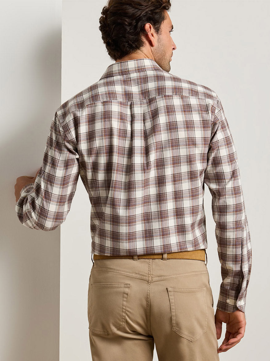 A man seen from the back wearing a white and brown plaid Peter Millar Cannon Performance Flannel Sport Shirt in Winter Ivory, tucked into tan trousers with a belt.