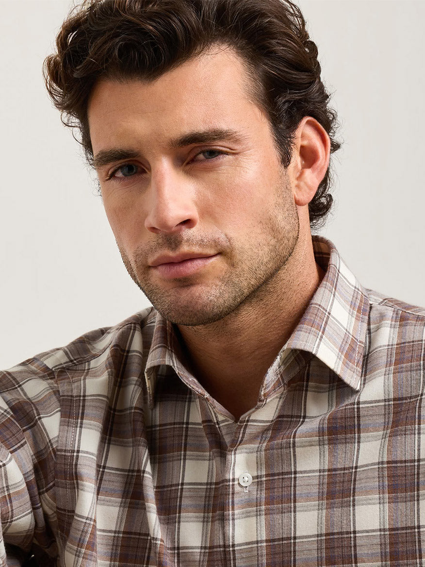A man wearing a Peter Millar Cannon Performance Flannel Sport Shirt in Winter Ivory, a lightweight, ivory and brown plaid flannel button-down.