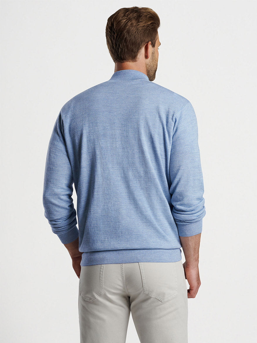 Man viewed from the back wearing a Peter Millar Canton Stripe Quarter-Zip Sweater in Cottage Blue and beige pants, standing against a plain white background.