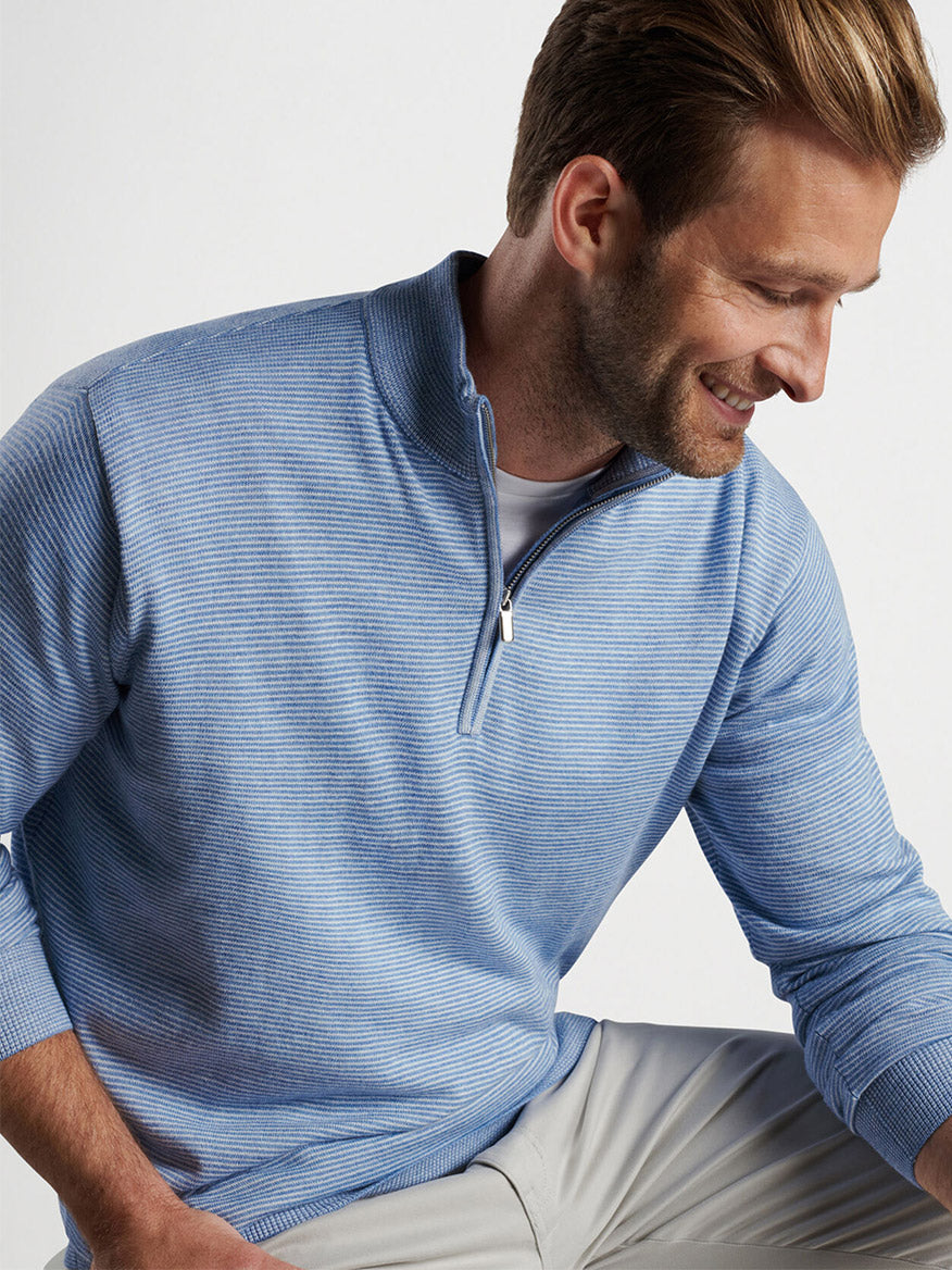 Smiling man in a Peter Millar Canton Stripe Quarter-Zip Sweater in Cottage Blue looking to the side, set against a light background.