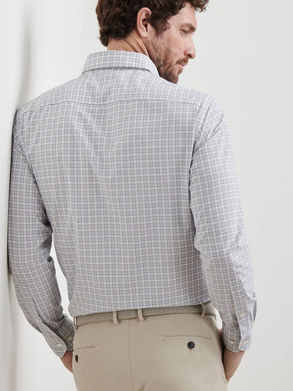 A man is seen from behind wearing a Peter Millar Carter Performance Poplin Sport Shirt in Nebula Blue, long-sleeved and tucked into beige pants with a woven belt.