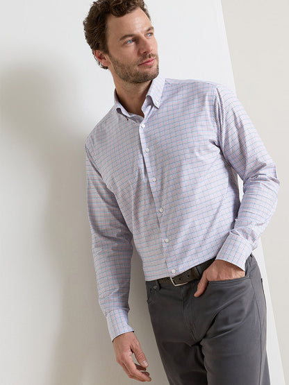 A man wears the Peter Millar Casey Performance Twill Sport Shirt in navy with gray pants, standing against a white wall, one hand in his pocket.