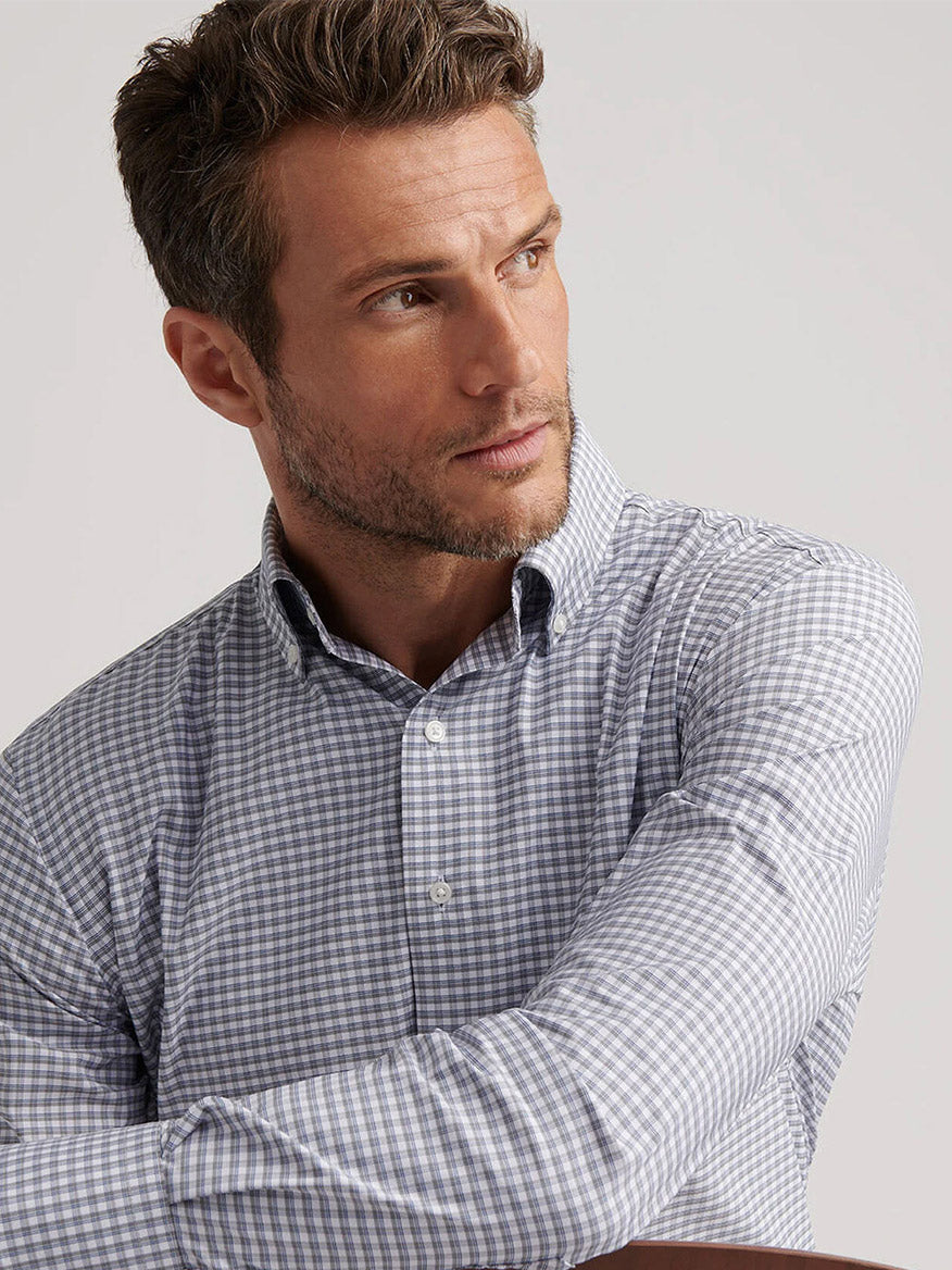 A man wearing the Peter Millar Cashiers Performance Twill Sport Shirt in Oslo Grey, featuring a light gray and white check pattern and classic fit, looks to his left against a plain background.