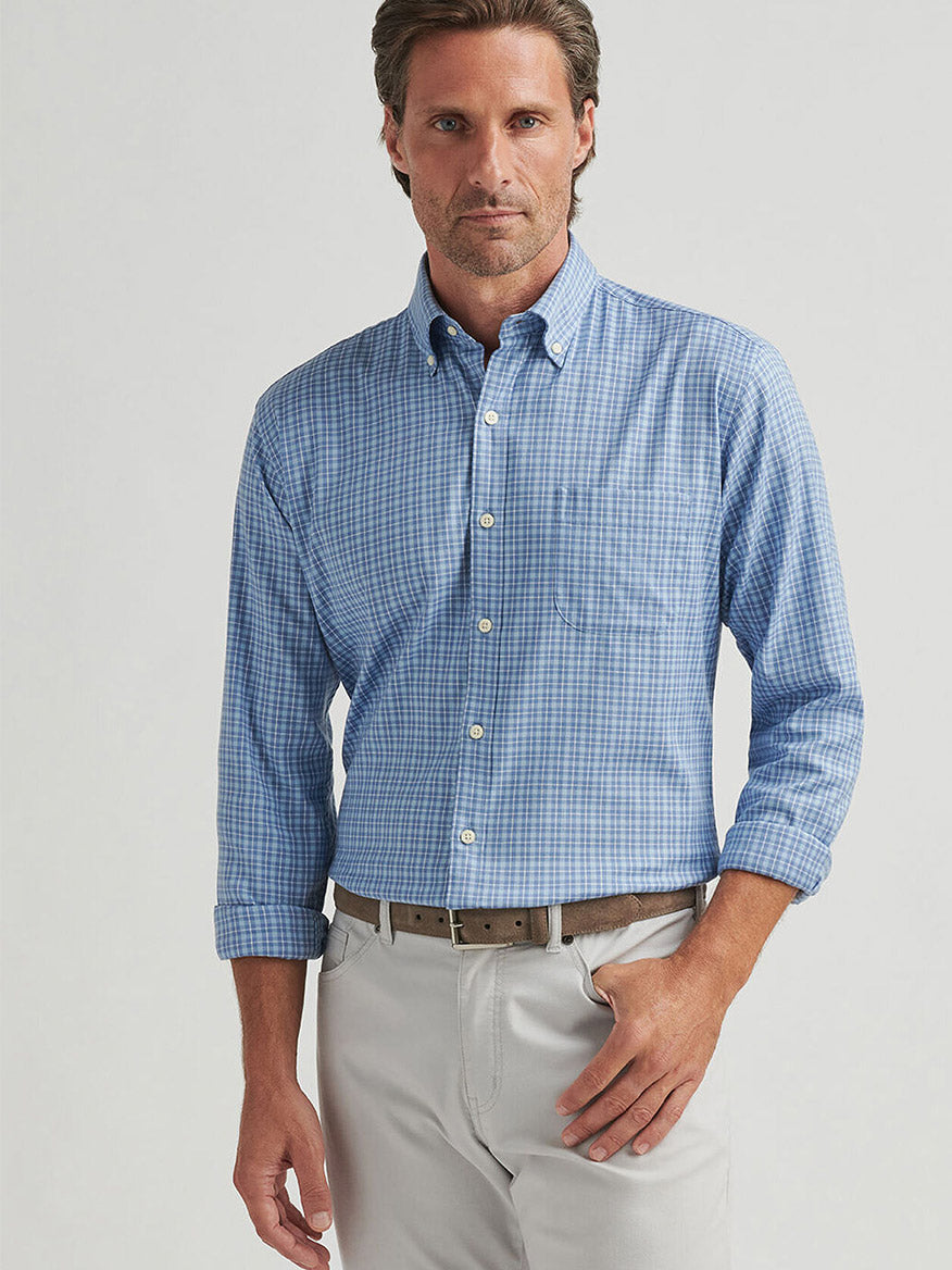 A man wearing the Peter Millar Caspian Perfect Pinpoint Cotton-Stretch Sport Shirt in Blue Freesia and light pants stands against a plain background, showcasing a casual yet polished style.