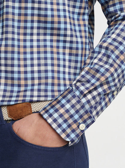 A person is sporting the Peter Millar Chambly Crown Lite Cotton-Stretch Sport Shirt in Navy, showcasing an easy-care plaid design in blue and brown hues, with a hand nonchalantly tucked in a pocket. The shirt provides UPF 50+ sun protection, making for an ideal pairing with a subtly shown belt and dark blue pants.