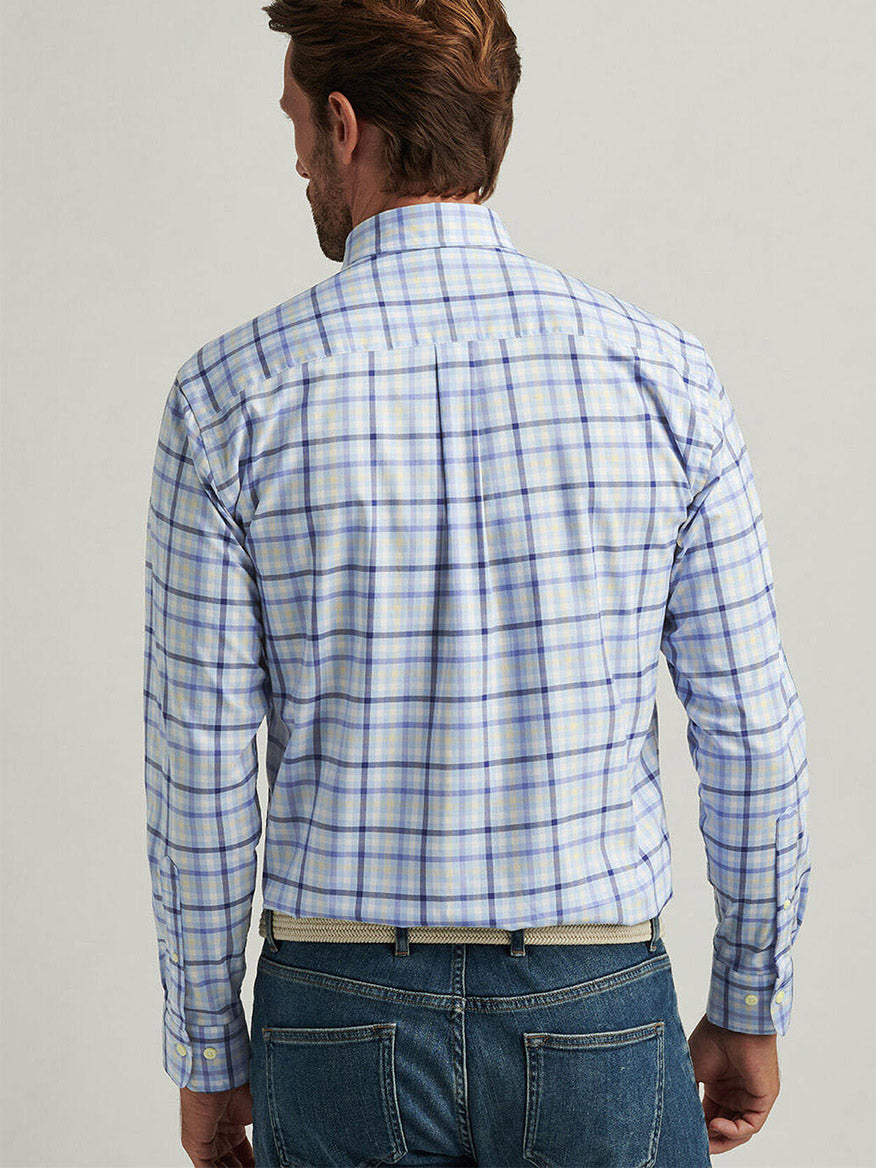 A man is seen from the back wearing the Peter Millar Chambly Crown Lite Cotton-Stretch Sport Shirt in Morning Blue, featuring a classic fit and blue-and-white plaid design, paired with jeans.