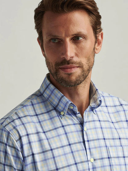 A man with short hair and a beard wears the Peter Millar Chambly Crown Lite Cotton-Stretch Sport Shirt in Morning Blue, featuring a classic fit and easy-care blue and yellow plaid fabric, as he looks to the side.